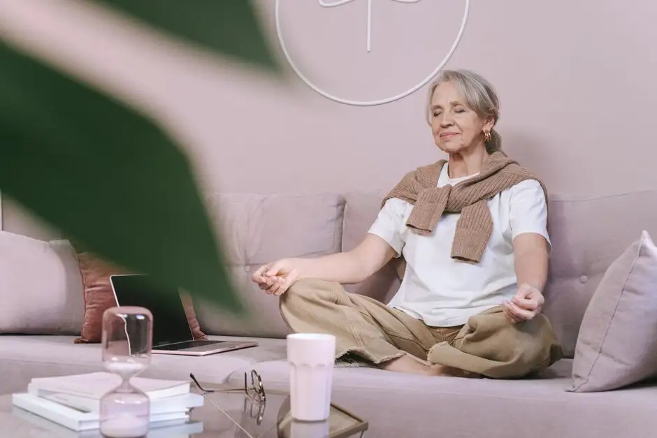 Personne assise en tailleur sur un tapis, yeux fermés, dans un salon lumineux et calme
